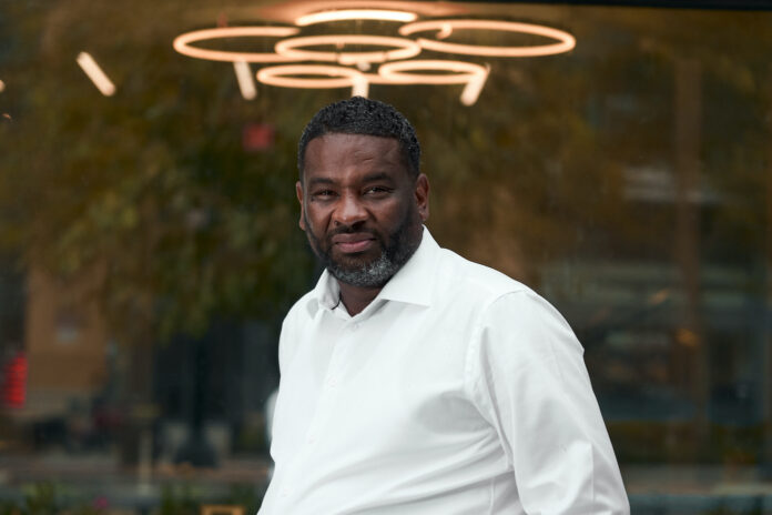 Monko CEO Terrence White in a white business shirt standing in front of a dispensary window with lights above his head Captured by Immanuel Powell Captured by Immanuel Powell