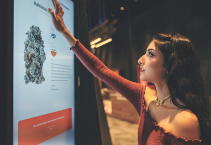 Woman with red shirt and brown hair reaching up to touch a Dispensary Interactive Menu