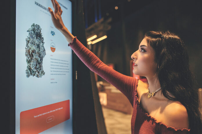 Woman with red shirt and brown hair reaching up to touch a Dispensary Interactive Menu