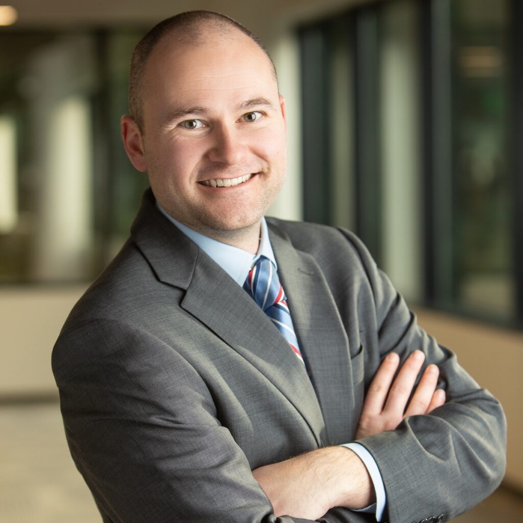 Brett Ballman headshot businesses man in suite and tie with arms crossed smiling