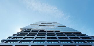 8 Things to Know About Cannabis REITs POV looking up at a large skyscraper with glass windows and a blue sky with clouds