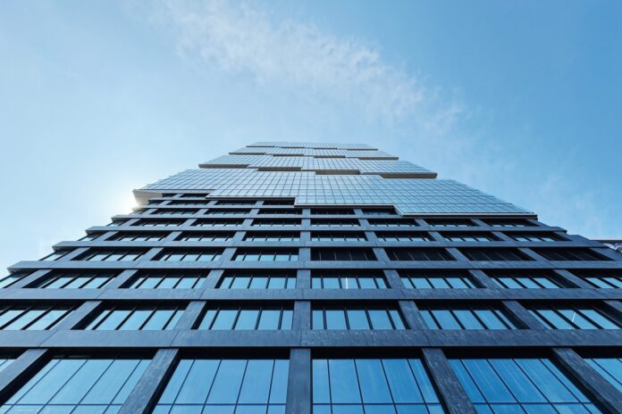 POV looking up at a large skyscraper with glass windows and a blue sky with clouds