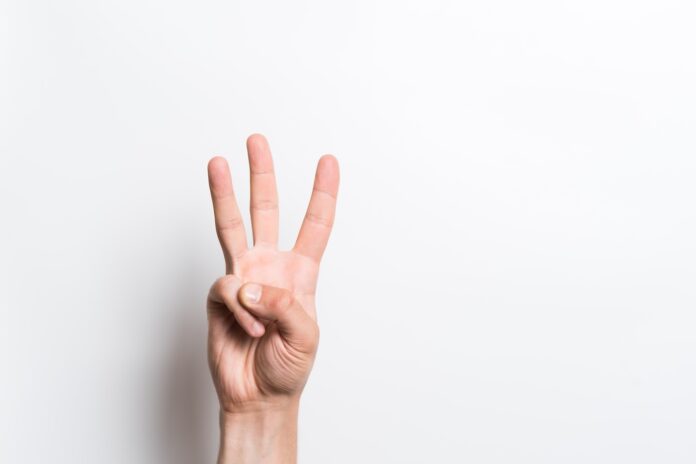 Photo of a Caucasian male hand showing the gesture of the number three with three fingers pointed up. Shot on white background.