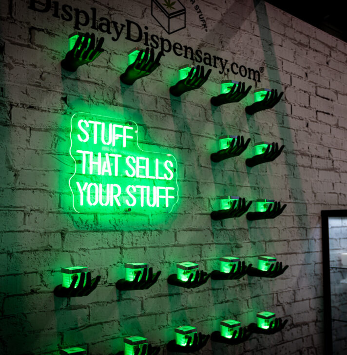 A wall display featuring neon-lit hands holding small product containers, with a glowing green neon sign that reads &quot;Stuff That Sells Your Stuff.&quot;