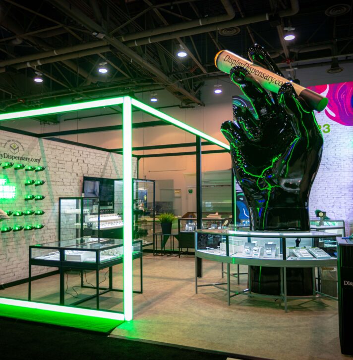 Display Dispensary booth showcasing a large black hand sculpture, neon lighting frames, and modern product displays.