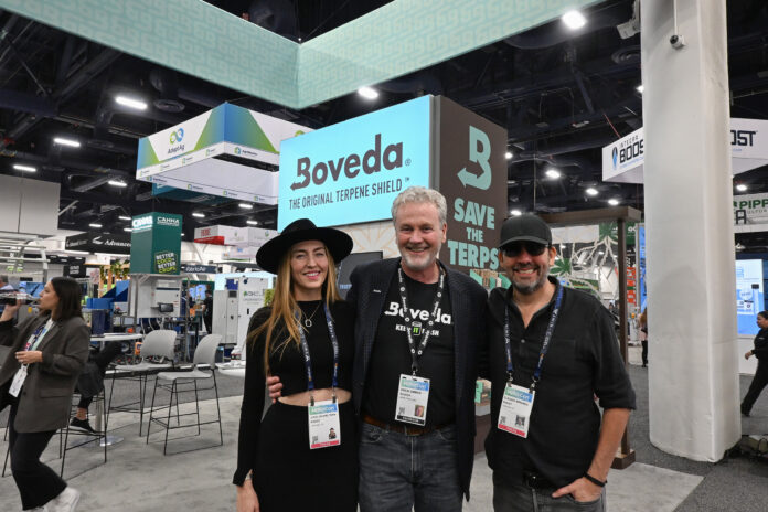 Boveda representatives at MJBizCon 2024, standing in front of their booth showcasing the Original Terpene Shield with the "Save the Terps" slogan.