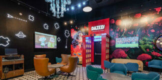 Inside Planet 13’s Dazed Consumption Lounge The interior of Dazed Consumption Lounge at Planet 13 Las Vegas, featuring futuristic neon wall designs, plush seating, and a vibrant mural with a surreal forest scene.