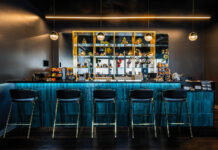 The Artist Tree Elevates Cannabis Culture with Art and Community Modern bar area at The Artist Tree Cannabis Lounge in Hawthorne, California, featuring sleek turquoise tile, brass accents, and curated shelving with art and cannabis accessories.