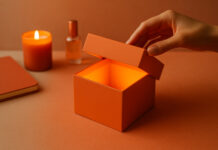 Packaging: the Trojan Horse of Cannabis Branding A hand opens a glowing orange box surrounded by a candle, journal, and glass bottle, symbolizing the emotional and aesthetic experience of modern cannabis packaging.