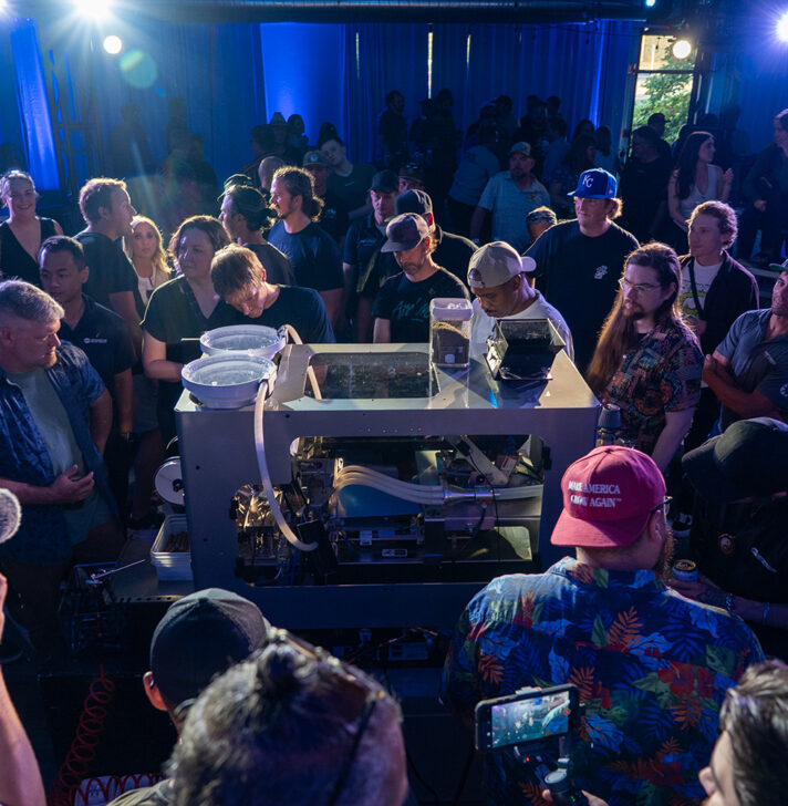 Crowd closely observes the RollPros Blackbird XXL blunt-rolling machine demo