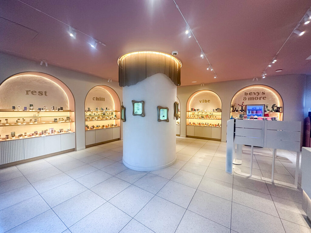 Wide view of Alta Dispensary’s arched product displays labeled “rest,” “chill,” “vibe,” and “bevys & more” with illuminated shelving and central column.