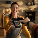More Than a POS: Mariner’s Human-First Tech Solutions Smiling retail worker handing a customer a POS terminal for payment, symbolizing Mariner Business Solutions’ human-centered technology and service.