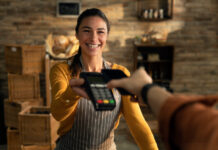 More Than a POS: Mariner’s Human-First Tech Solutions Smiling retail worker handing a customer a POS terminal for payment, symbolizing Mariner Business Solutions’ human-centered technology and service.