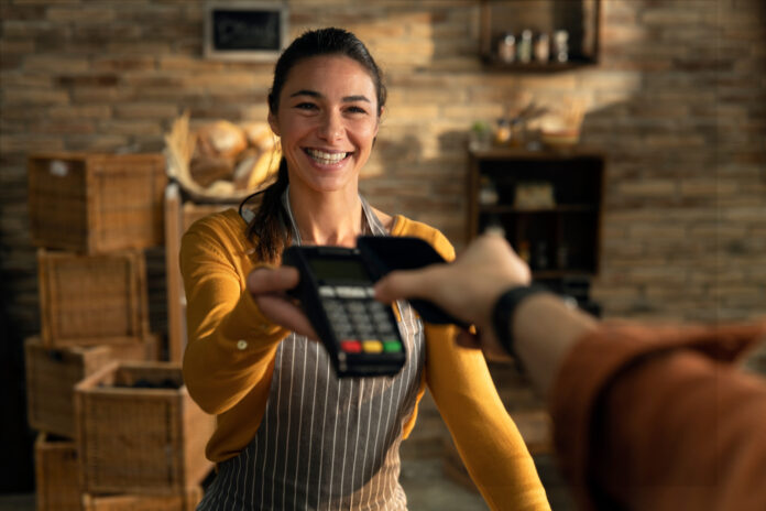 Smiling retail worker handing a customer a POS terminal for payment, symbolizing Mariner Business Solutions’ human-centered technology and service.
