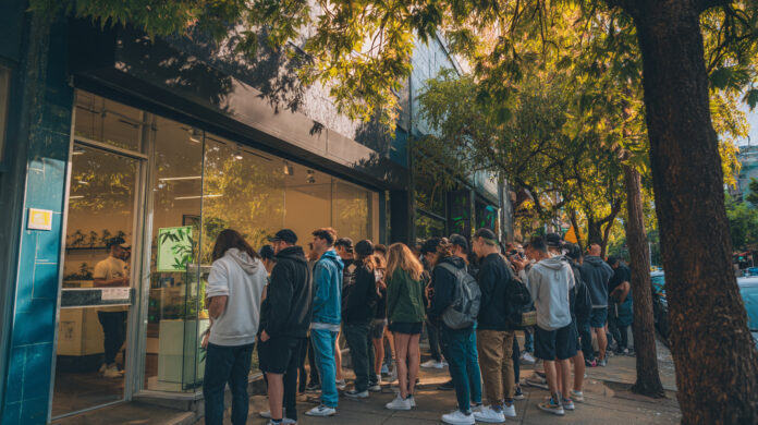 Customers line up outside a modern cannabis dispensary in a bustling urban area, highlighting foot traffic and tourist interest.