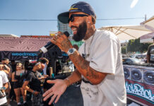 Weedmaps Hosts Star-Studded Kickback Event with DJ Mustard and Larry June Performer with microphone engaging the crowd during a live set at Weedmaps Kickback LA, with Weedmaps branding and DJ booth in background.