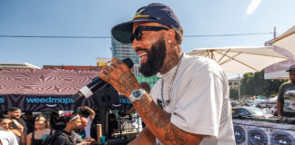Weedmaps Hosts Star-Studded Kickback Event with DJ Mustard and Larry June Performer with microphone engaging the crowd during a live set at Weedmaps Kickback LA, with Weedmaps branding and DJ booth in background.