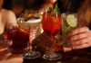 Alcohol Sales Slide While Cannabis Drinks Surge Toward $2.8B Market Four people clink colorful sparkling beverages in elegant glassware at a warm, upscale setting, symbolizing the shift toward low- and no-alcohol and cannabis-infused drink trends.