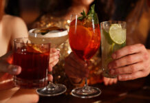 Alcohol Sales Slide While Cannabis Drinks Surge Toward $2.8B Market Four people clink colorful sparkling beverages in elegant glassware at a warm, upscale setting, symbolizing the shift toward low- and no-alcohol and cannabis-infused drink trends.
