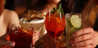 Alcohol Sales Slide While Cannabis Drinks Surge Toward $2.8B Market Four people clink colorful sparkling beverages in elegant glassware at a warm, upscale setting, symbolizing the shift toward low- and no-alcohol and cannabis-infused drink trends.