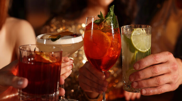 Alcohol Sales Slide While Cannabis Drinks Surge Toward $2.8B Market Four people clink colorful sparkling beverages in elegant glassware at a warm, upscale setting, symbolizing the shift toward low- and no-alcohol and cannabis-infused drink trends.