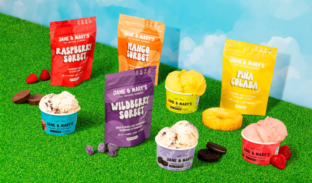 Colorful display of Jane & Mary’s THC-infused ice cream and sorbet cups arranged on bright green turf with matching gummy pouches in the background.