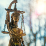 DoJ Shift: Stricter Marijuana Enforcement on Federal Lands lClose-up of a Lady Justice statue with sunlight flaring behind it, symbolizing federal law and policy.