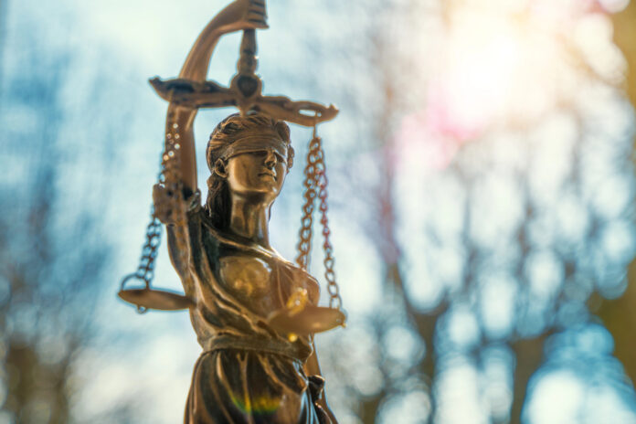lClose-up of a Lady Justice statue with sunlight flaring behind it, symbolizing federal law and policy.