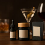 Living Near Dispensaries Linked with More Cannabis Use, Less Heavy Drinking Minimalist product packaging in focus with blurred alcoholic drinks behind it on a warm bar surface.