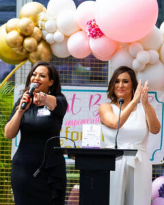 Blunt Brunch founders Parisa Rad and Adelia Carillo speaking at a podium during the 2024 national event, framed by pink and gold balloon decor, highlighting leadership and community engagement.