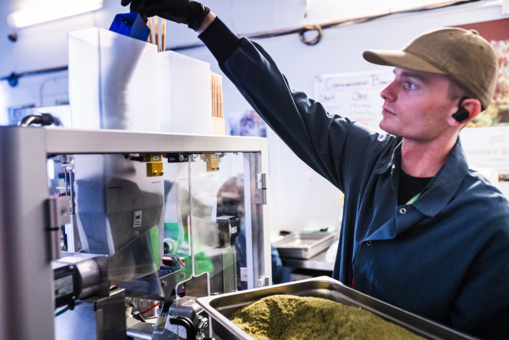 A technician loading materials into a Hefestus automated pre-roll system inside a production facility.