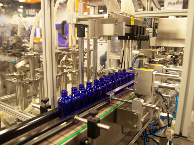 Pack Leader USA automated cannabis oil filling machine dispensing into blue glass bottles at MJBizCon 2025.