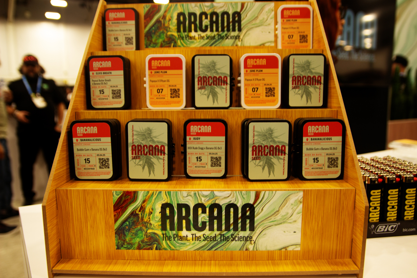 Arcana Seed booth at MJBizCon 2025 featuring labeled cannabis seed tins and branded packaging.