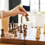 5 Essential Strategies from Leading Cannabis PR Agencies A hand moves a chess piece on a wooden chessboard, symbolizing strategic planning in cannabis public relations and earned media.