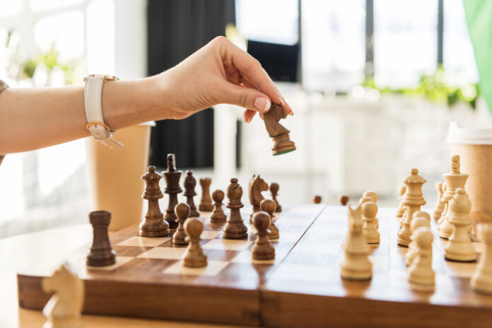 A hand moves a chess piece on a wooden chessboard, symbolizing strategic planning in cannabis public relations and earned media.