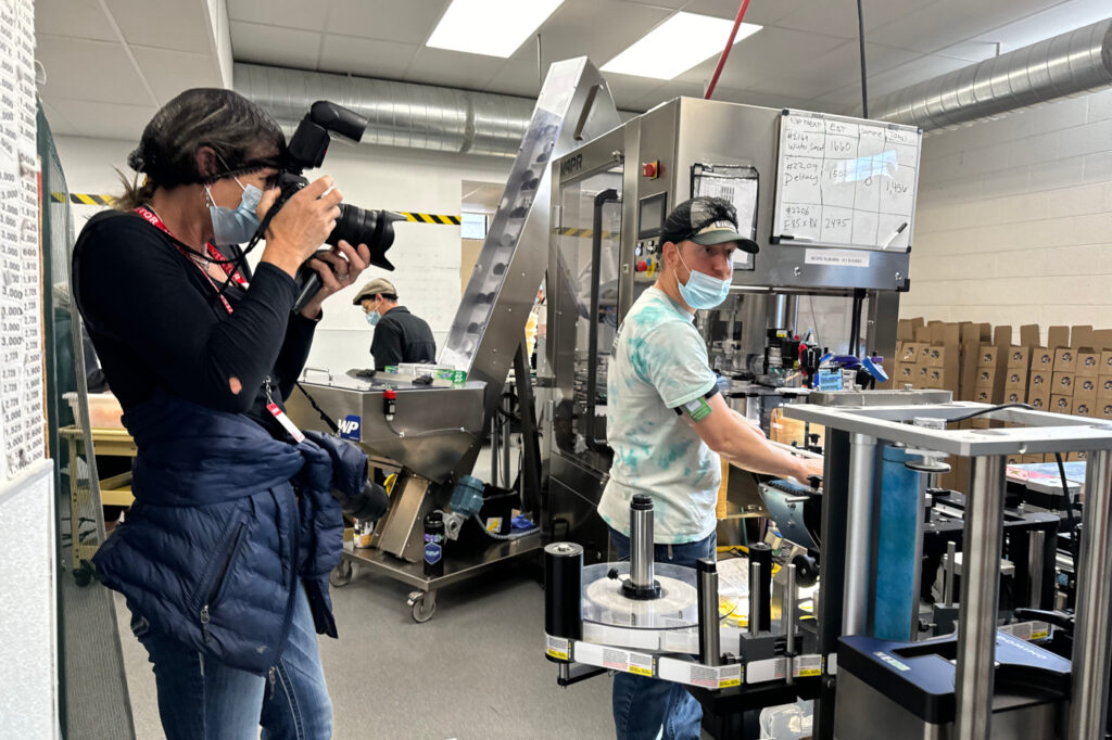 A photographer documents a subject in a production facility, illustrating earned media storytelling in an operational environment.