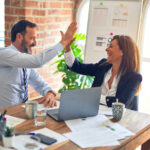 Maverick PR on Trust, Patience, and Credibility in Regulated Markets Two business professionals share a celebratory high-five during a meeting, symbolizing trust, collaboration, and successful partnership.
