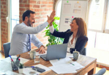 Maverick PR on Trust, Patience, and Credibility in Regulated Markets Two business professionals share a celebratory high-five during a meeting, symbolizing trust, collaboration, and successful partnership.