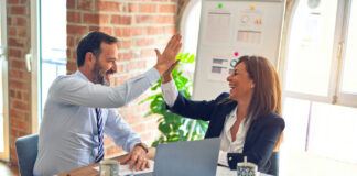 Maverick PR on Trust, Patience, and Credibility in Regulated Markets Two business professionals share a celebratory high-five during a meeting, symbolizing trust, collaboration, and successful partnership.