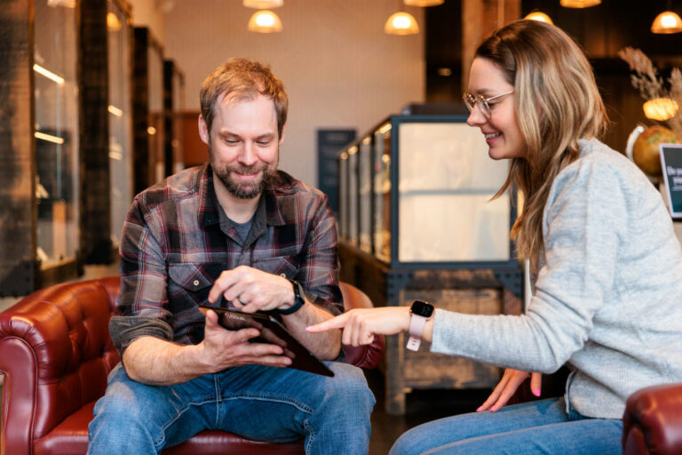 A budtender and customer sitting on a couch in a modern dispensary, demonstrating a simplified and empathetic cannabis retail experience.