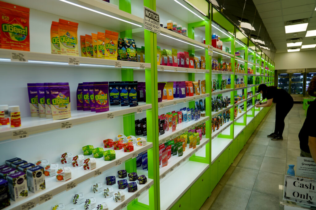 A staff member stocks products along a brightly lit aisle at GreenPharms in Mesa, Arizona.