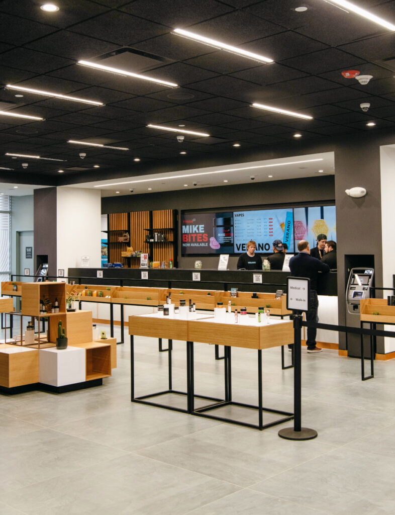 Wide view of a Zen Leaf dispensary sales floor with wood display tables and staff assisting customers near the service counter.