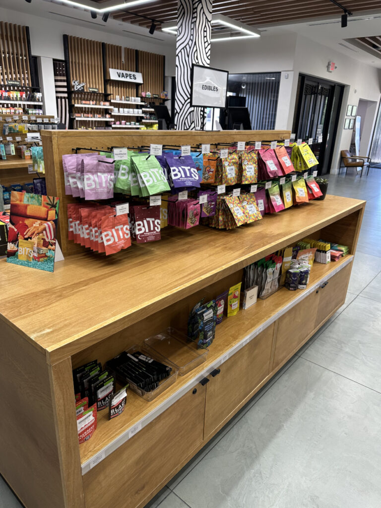 Colorful edible product packages displayed on a Zen Leaf merchandising fixture with wood shelving and category signage in the background.