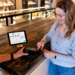 Why Most Cannabis Tech Sucks (and What Retailers Should Demand Instead) A budtender and customer smiling during a transaction using Cova’s dispensary POS system.
