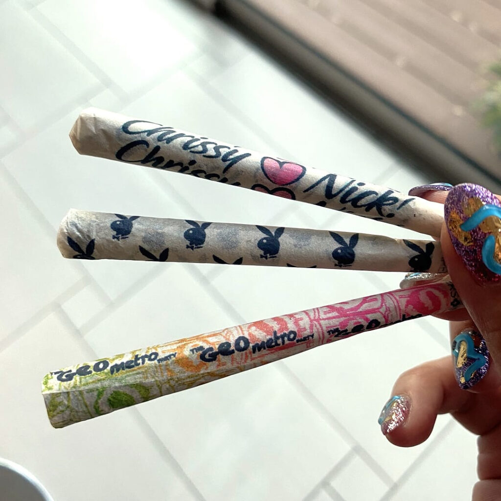 Three custom-printed pre-roll cones held in a hand with patterned designs