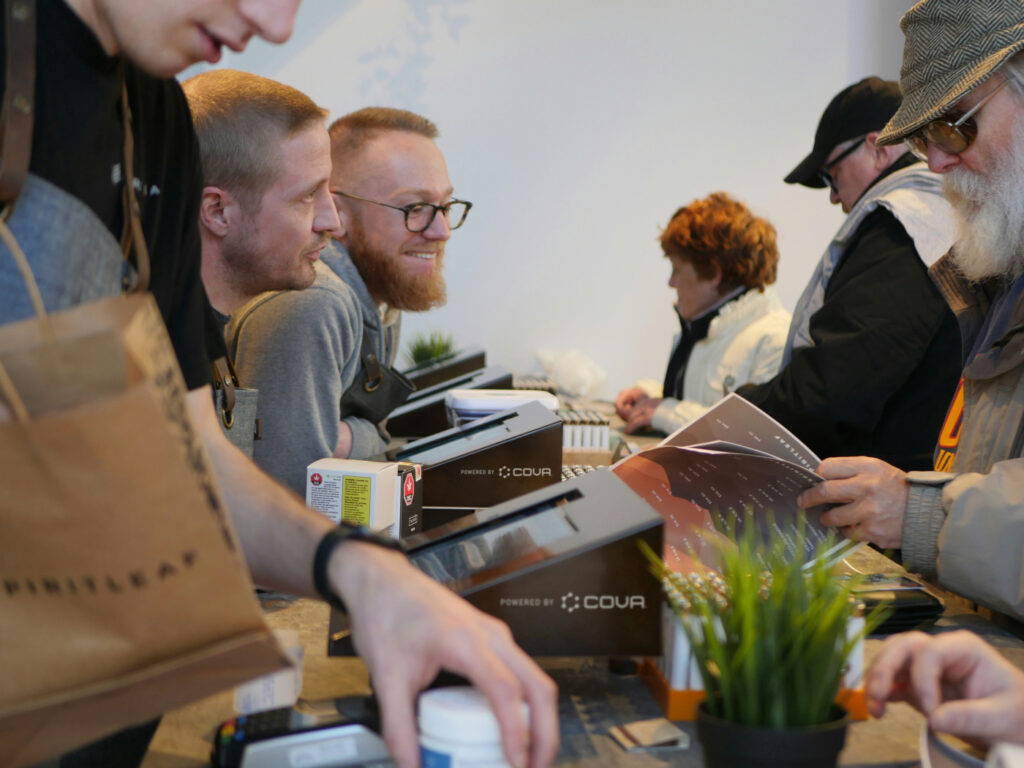 Dispensary staff assisting customers at a checkout counter during a busy retail shift.