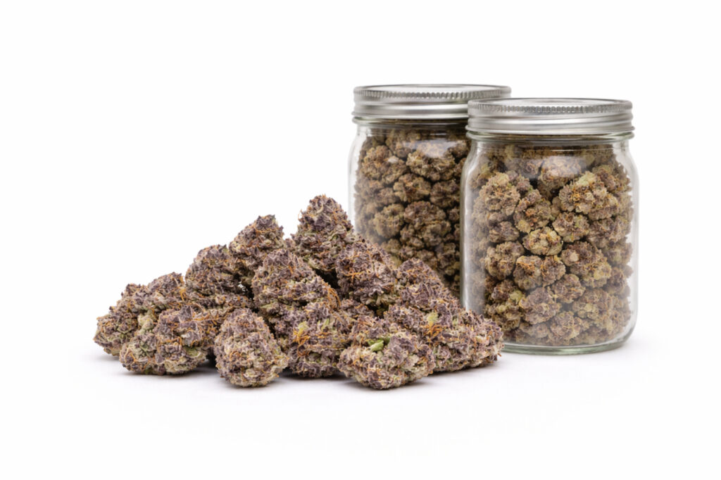 A pile of cannabis buds with two mason jars behind it on a white background.