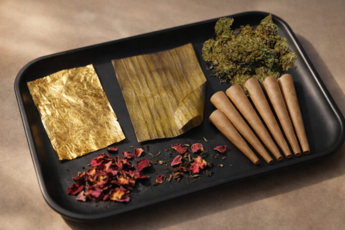 Shine 24K gold rolling papers, Million Bananas organic banana leaf wraps, and Botani tea leaf wraps displayed with pre-rolled cones and cannabis flower on a tray.