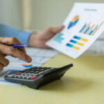 California Cannabis Tax Revenue Dips in Q4 2025 Person using a calculator beside printed charts, illustrating California cannabis tax revenue totals for Q4 2025.