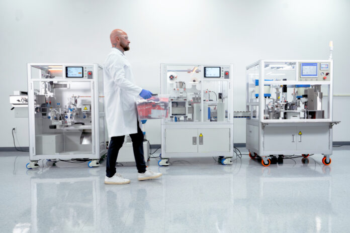 Technician operating an automated vape cartridge packaging line in a clean manufacturing room.